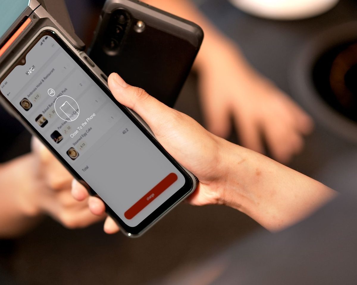 A stallholder holding out their phone while a customer taps their own phone against it to pay