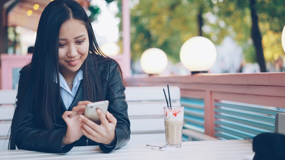 A woman smiling at her phone at an outdoor café