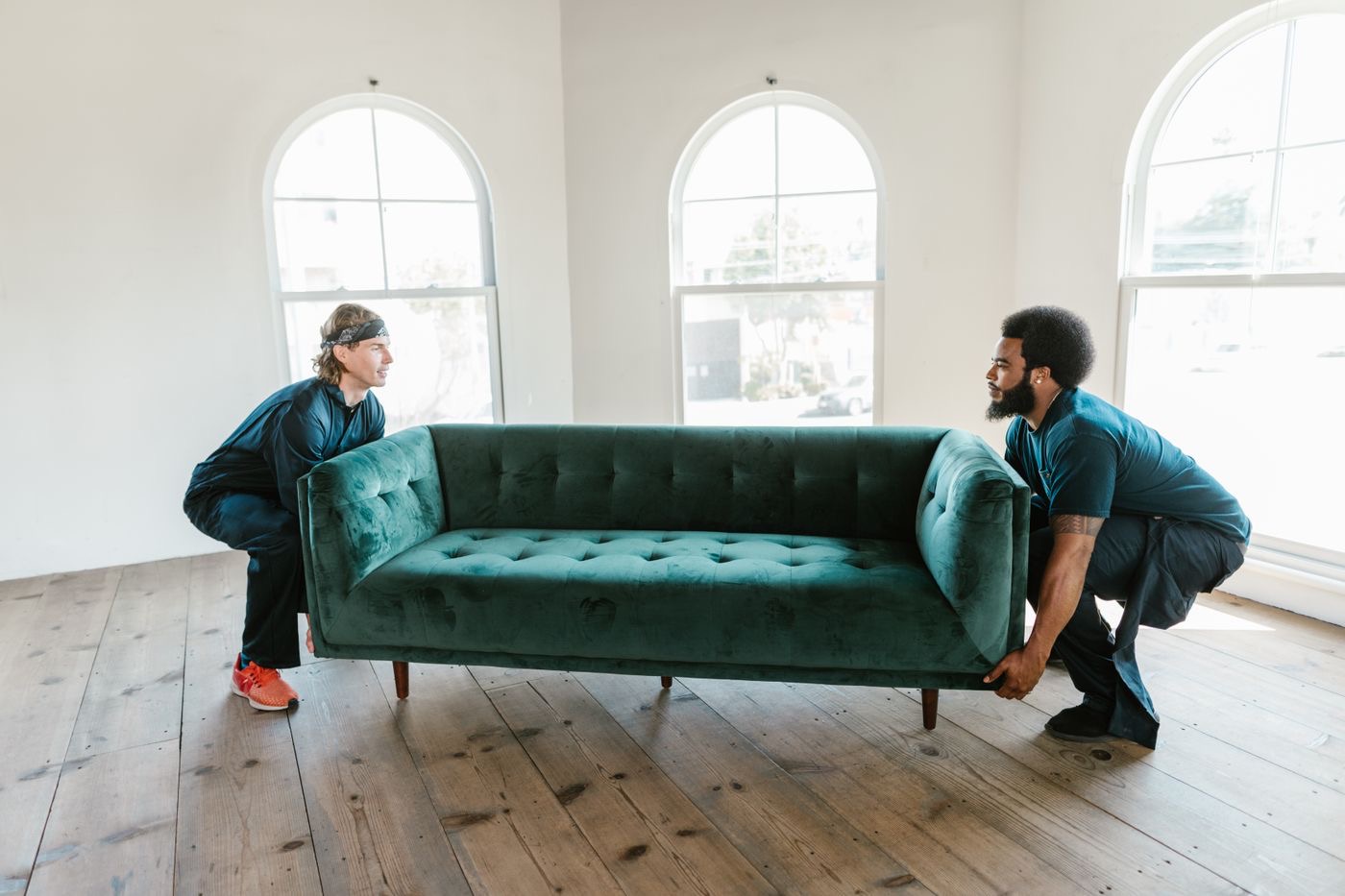 Two men carrying a green sofa across a sunlit room